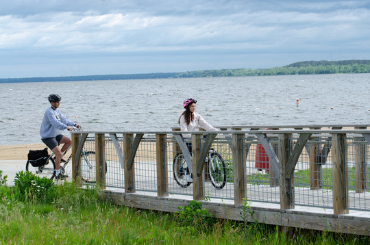 Two young adults biking on a bridge on a state trail by the lake on an overcast day.