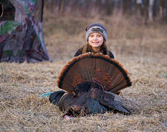 turkey hunter, a young kid, near a blind and she's holding the turkey she harvested