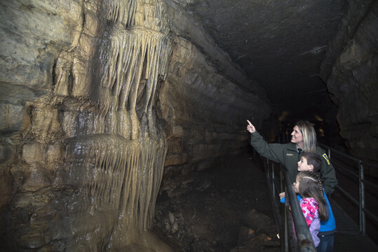 Park naturalist pointing at cave formation for two young kids visiting the cave.
