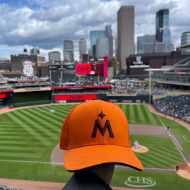 Twins cap in orange with field in the background and downtown Minneapolis beyond that