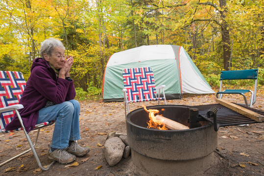 Female camper on chair by fire pit, tent  seen in the background.
