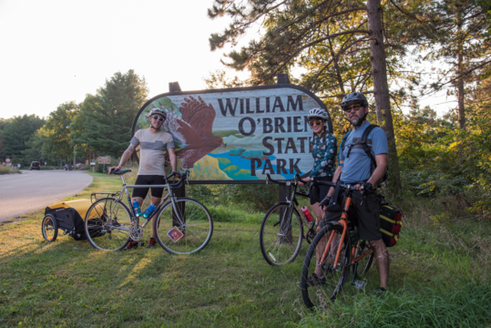 Three cyclists posing by William O'Brien State Park entrance sign.