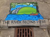 Storm drain with The River Starts Here art