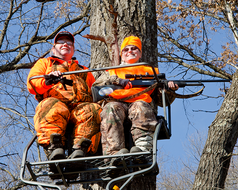 two deer hunters in blaze orange in a tree stand