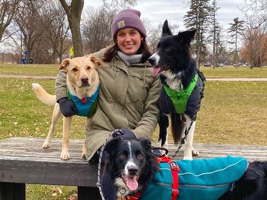 A woman in a coat with three dogs