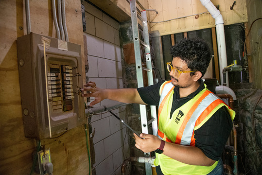 A man in a safety vest inspects an electrical panel