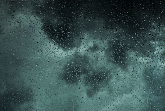 Dark and stormy clouds with raindrops on a window pane