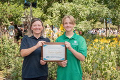 A woman and a teenager holding a plaque in front of a garden