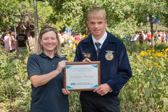 A woman and a teenager holding a plaque in front of a garden