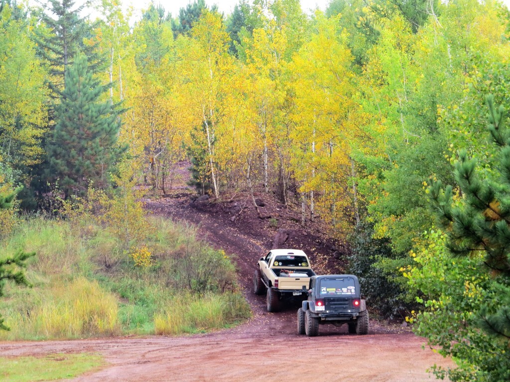 Two off-highway vehicles on a mud trail surrounded by bright yellow and green trees.