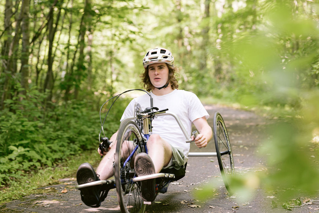 Man on adaptive bike on paved trail, surrounded by green.