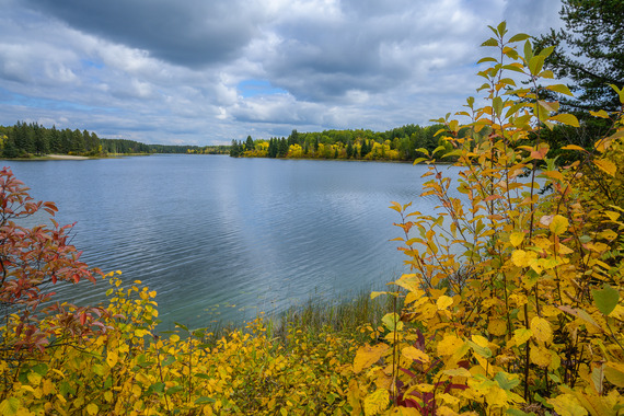 A calm lake with trees along the shore starting to change to fall colors.