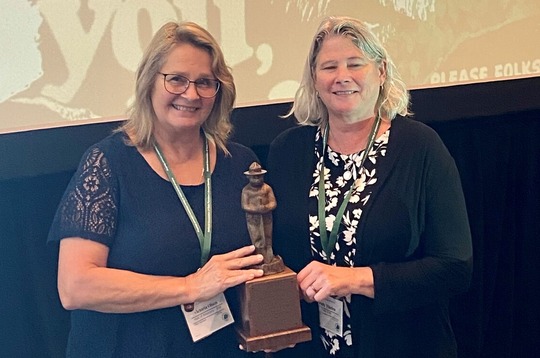 Two women hold an award with a Smokey Bear graphic projected behind them