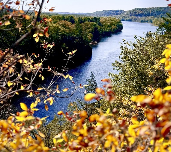 River framed by yellow and orange foliage, greens on the shore, and a blue sky.