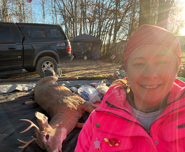 hunter in blaze pink with a buck on a trailer with a truck in the background, deer camp scene