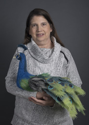 Artist posing with a felted sculpture of a peacock.