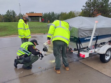 Three people in reflective vests inspect a boat for aquatic invasive species