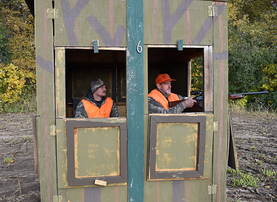 deer hunter in an enclosed blind with a non-hunting assistant sitting next to him