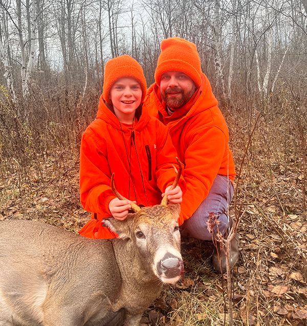 A young hunter with the deer he harvested, and an adult with him