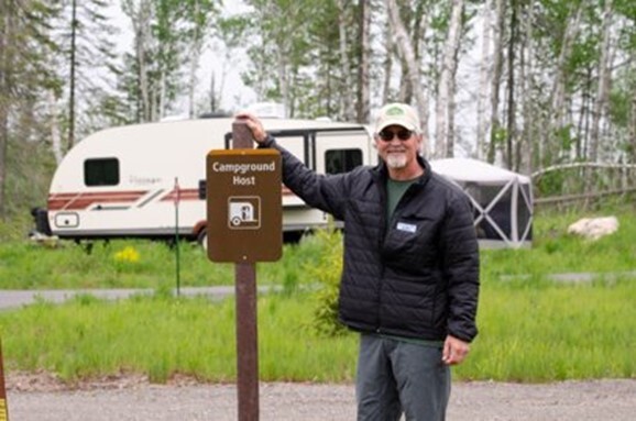 Man standing next to campground host sign