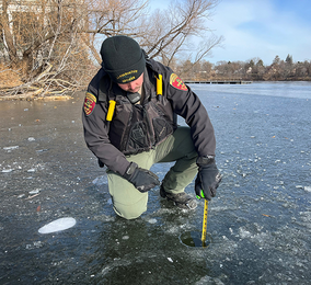 a DNR conservation officer measuring the ice with a tape measure, and ice is only a few inches thick