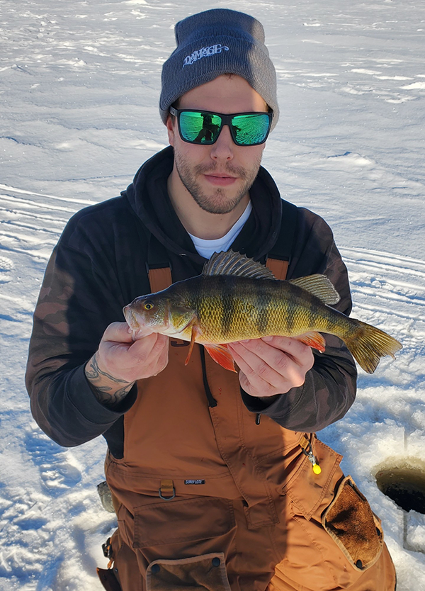 Angler in sunglasses kneeling on the Lake Superior ice holding a large perch