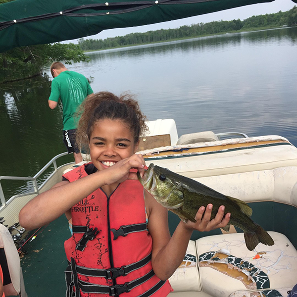 girl holding a bass she caught on a pontoon boat