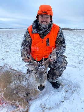 hunter in the snow with a buck he harvested with a muzzleloader