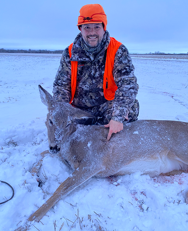 hunter with an antlerless deer he harvested, snowy scene in the background