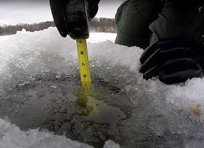 tape measure in a hole in the ice showing about 6 inches of ice