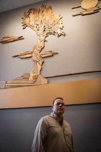 Man posing with his art, the Spirit Tree made out of wood.