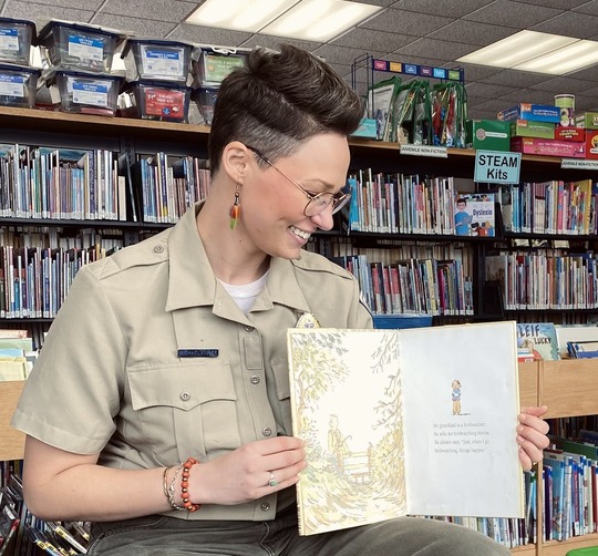 Naturalist in uniform holding book for story time at library.