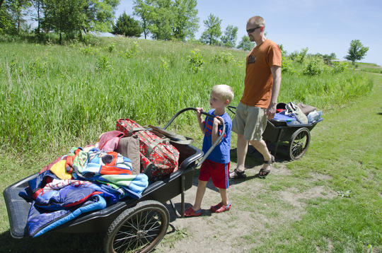 A parent and a child each pull a cart of camping gear to a cart-in campsite. 
