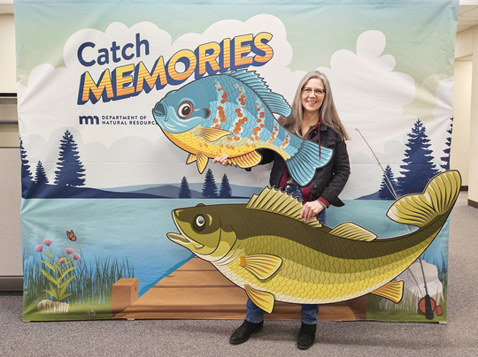 A woman holding cutouts of fish in front of a banner