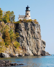 A lighthouse sits at the edge of a rock cliff on Lake Superior. 