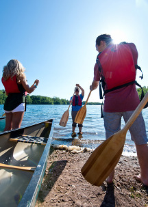 An instructor shows participants how to paddle a canoe on the shore of a lake. 