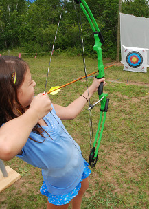 A teen shoots a bow and arrow at a circle target a few yards away. 