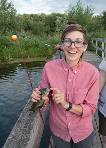 A person holds up a fish while standing on a fishing pier. 