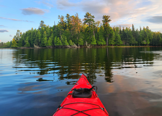 A red kayak floats on a calm lake at sunset. 