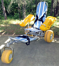 An adaptive chair that has flotation devices attached to the armrests sits on a sand beach. 