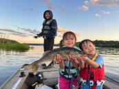 angler with two kids nearby on a boat holding a walleye