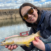 angler holding a trout by a stream