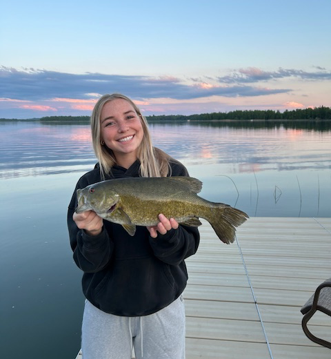 angler holding a smallmouth bass she caught off a dock