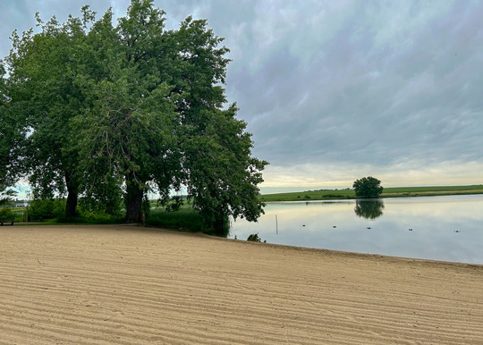 A groomed beach stretches out to a small pond in the countryside. 