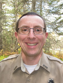 A person wearing a ranger uniform and glasses smiles at the camera. 