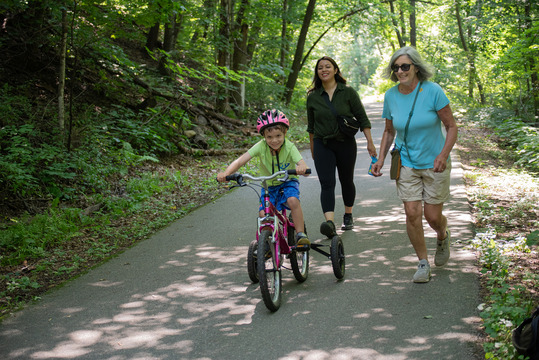 A boy on a bike with two people walking behind him