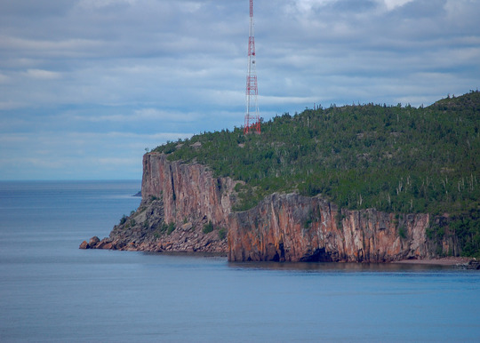 Looking down the shoreline of Lake Superior there is a tall radio tower on the horizon. 