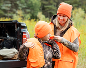 youth and adult as she helps the youth put on blaze orange next to the truck