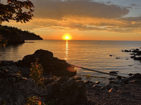 A glowing red sunset over Lake Superior is framed by leaves. 