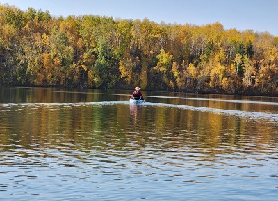 A person kayaks along a still lake in fall. 